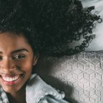 Beautiful black woman with curly hair smiling and lying on bed looking at the camera
